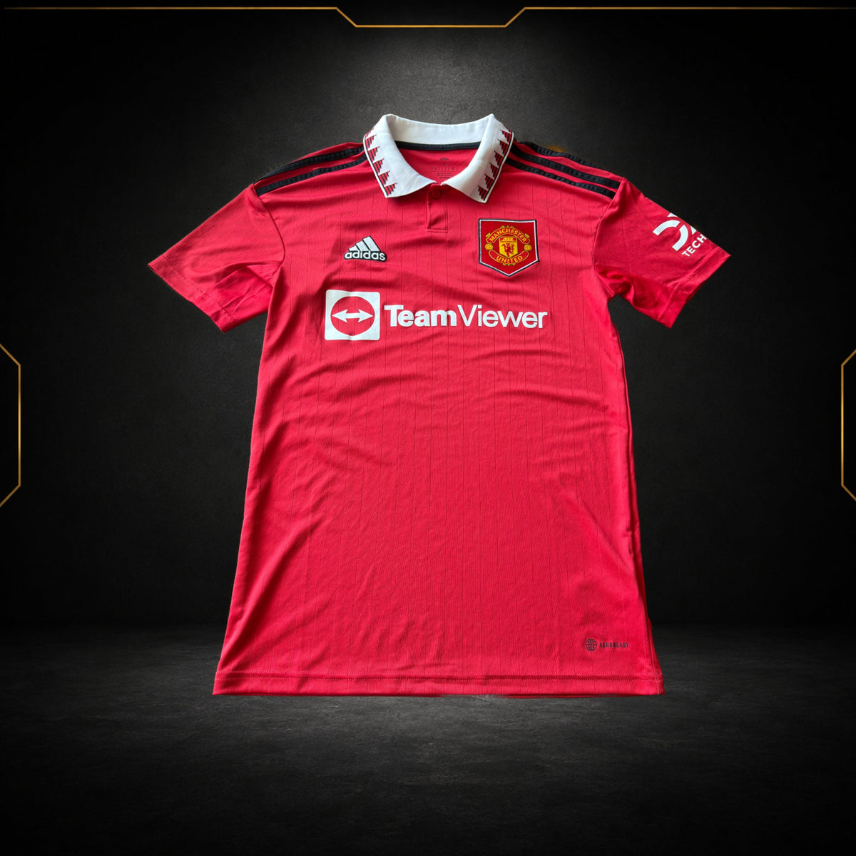 Originales rotes Manchester United Heimtrikot 2022/23, Vorderansicht auf schwarzem Hintergrund mit goldenen Akzenten von Maillots Market